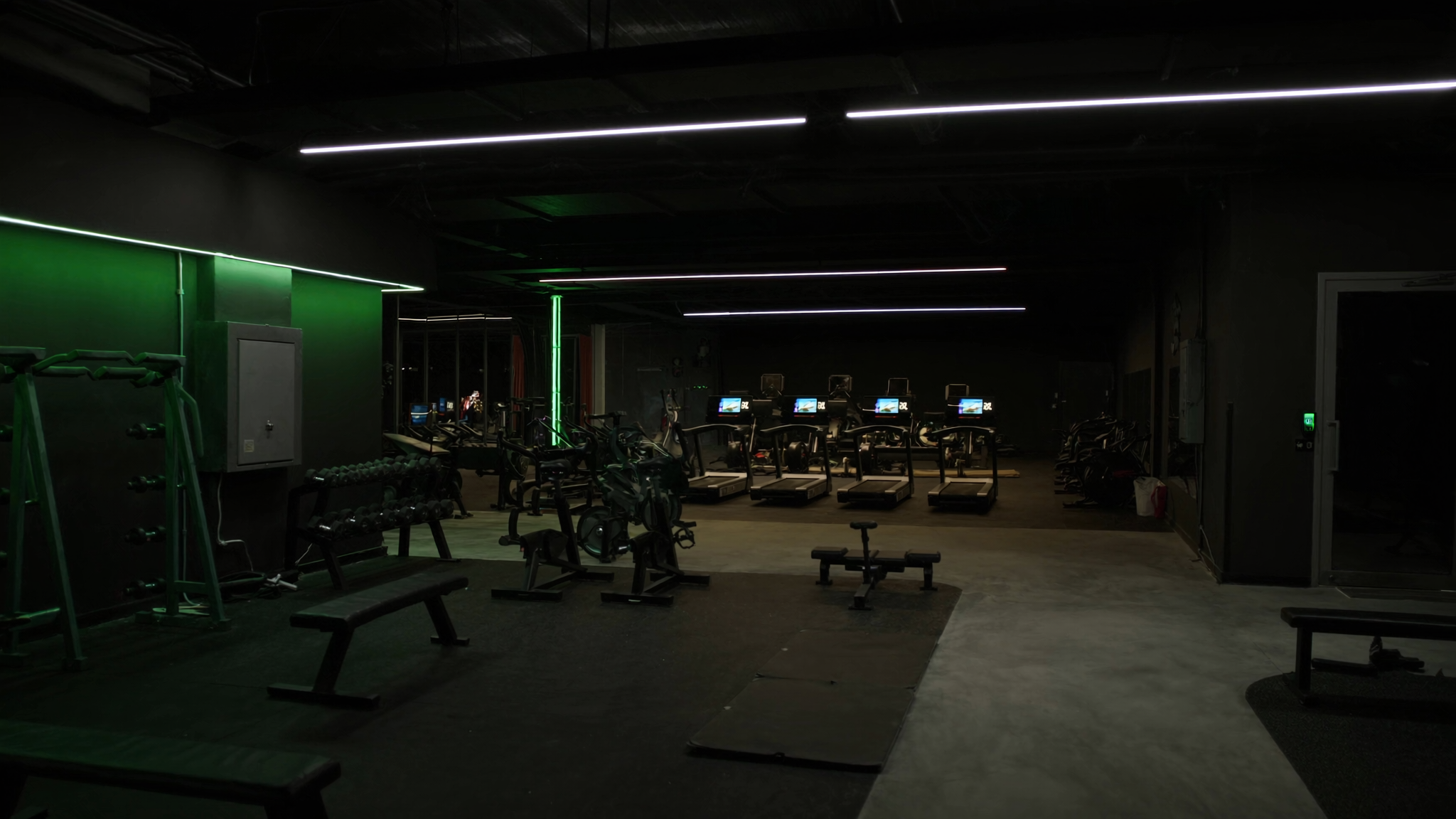 Tmavá hala fitness centra se zelenym osvětlením a chytrým vstupem